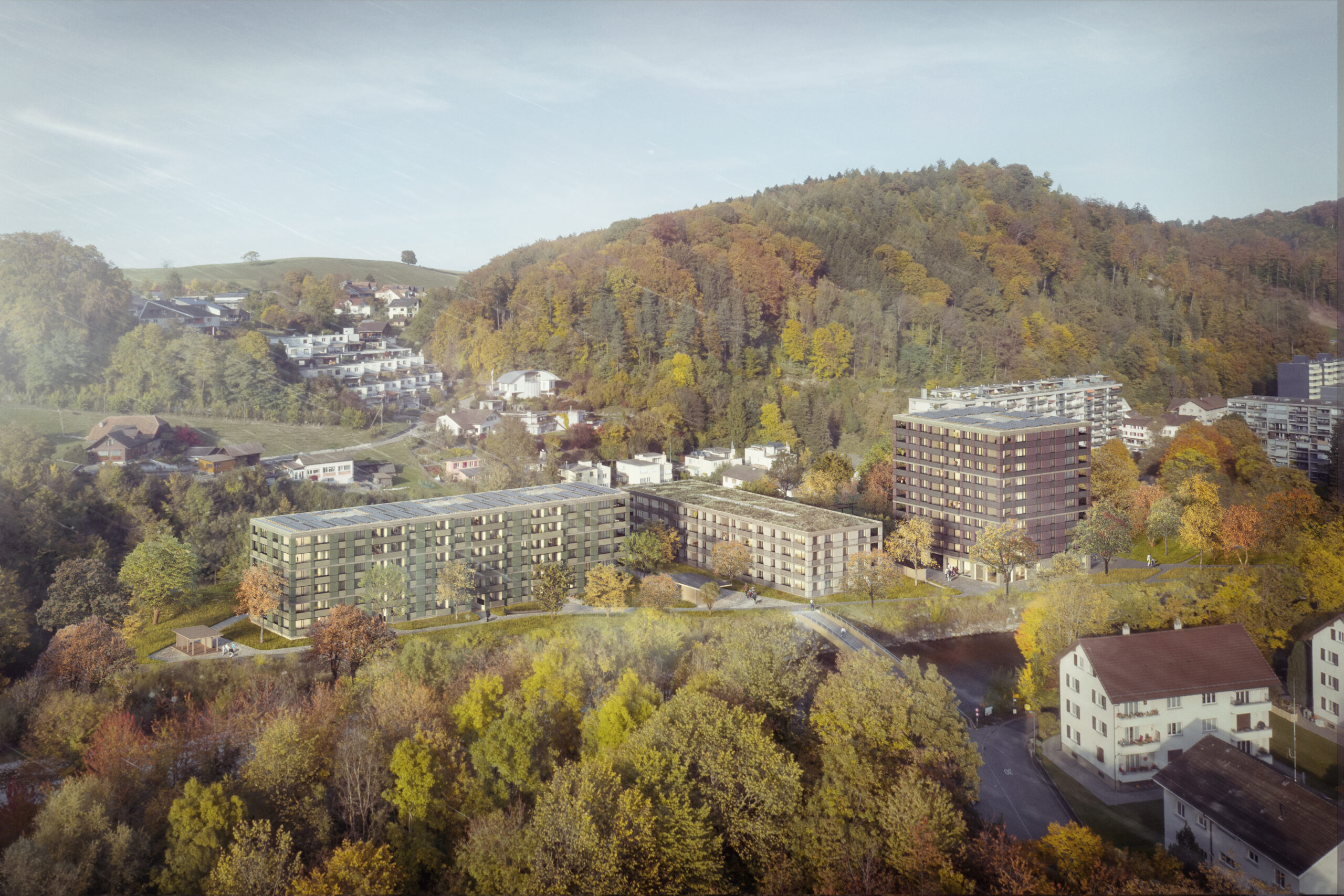 Luftaufnahme eines Wohngebiets, umgeben von üppigen, bunten Herbstbäumen und Hügeln. Mehrere moderne Wohnhäuser und einige Häuser sind zu sehen. Die Landschaft spiegelt eine Mischung aus Natur und Stadtentwicklung wider.