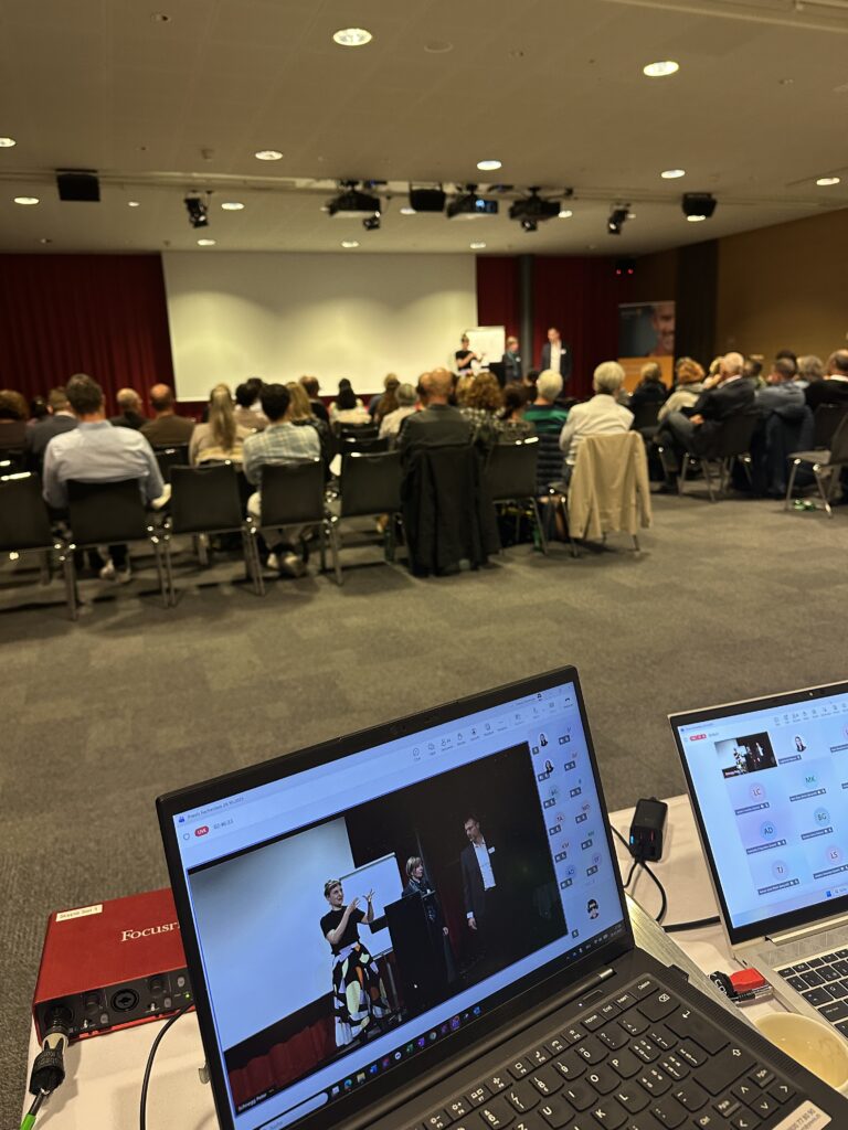 Fokus auf den Bildschirm, im Hintergrund ist der Vortragssaal ersichtlich.