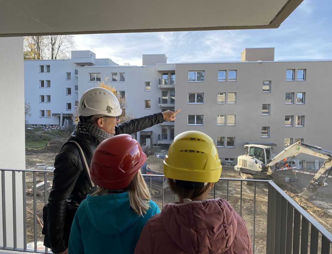 Der Projektleiter Immobilien steht mit zwei Schülerinnena uf einem Balkon und erklärt etwas zur Baustelle.